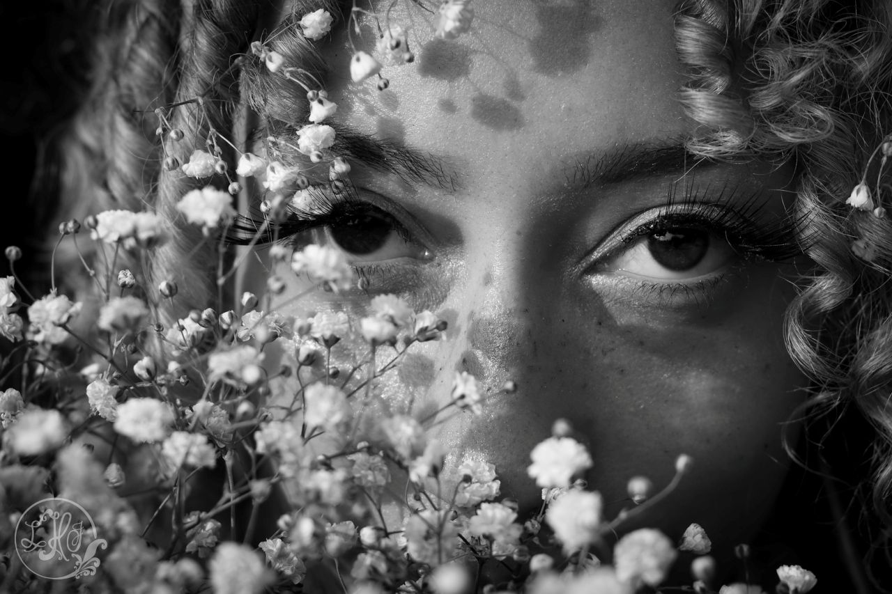 black and white photo of eyes behind flowers
